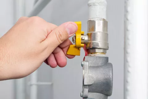Eine Hand dreht den Gas-Hahn an dem Heizungsrohr zu.